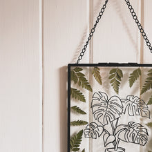 Load image into Gallery viewer, Top let angle of Handcrafted pressed flower frame featuring hand drawn Monstera Leaf. With fern leaves circling the drawing in a black glass frame, perfect for home decor