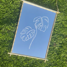 Load and play video in Gallery viewer, Brids eye view of Handmade mirror with a stunning hand-engraved Monstera leaf design, crafted from golden metal, combining functionality with artistic flair to brighten up any home.