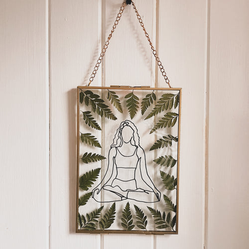 Handcrafted pressed flower frame featuring a drawing of a woman meditating, dried fern leaves inside the gold frame, perfect for home decor.