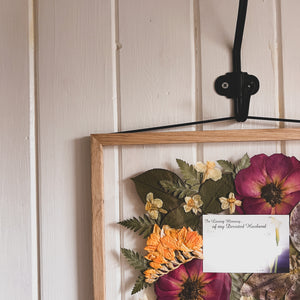 A close up of handcrafted pressed flower frame featuring  a sympathy card with pressed flowers around it., perfect for home decor.