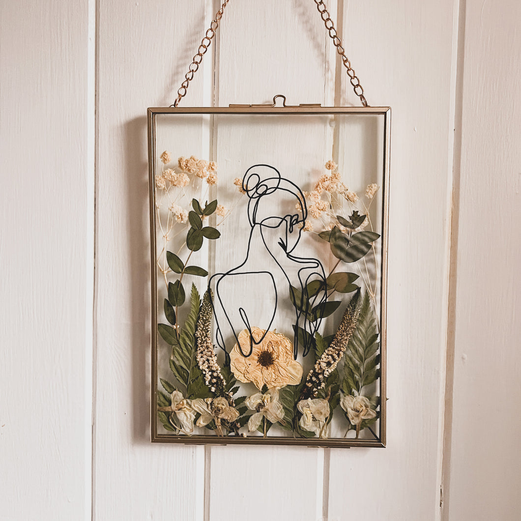 Handcrafted pressed flower frame featuring hand drawn back of a woman. With fern leaves and flowers in a gold glass frame, perfect for home decor