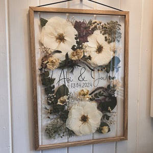 Side angle of handcrafted pressed flower frame for wedding preservation. Handwritten couples name and date featured. With a wedding bouquet secured in place, perfect for home decor.