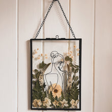 Load image into Gallery viewer, Handcrafted pressed flower frame featuring hand drawn back of a woman. With fern leaves and flowers in a black glass frame, perfect for home decor
