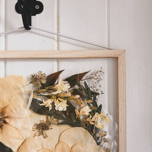 A close up of the corner of handcrafted pressed flower frame featuring a bridal bouquet which has carefully be pressed into a Ash wood frame.