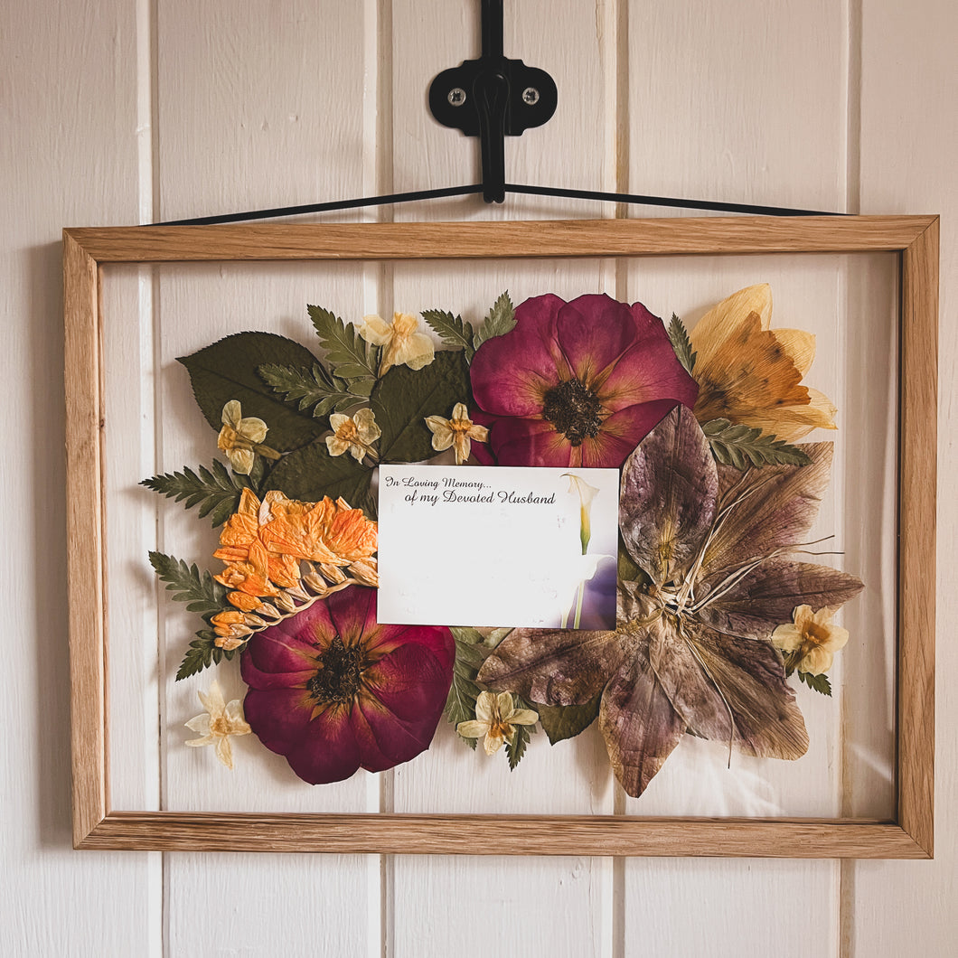 Handcrafted pressed flower frame featuring a sympathy card with pressed flowers around it.